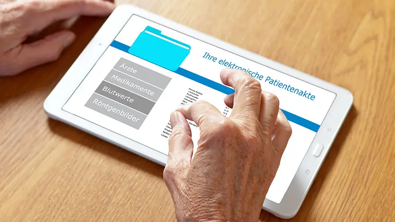 Hände eines Senioren über einem Tablet, auf dessen Bildschirm eine elektronische Patientenakte geöffnet ist