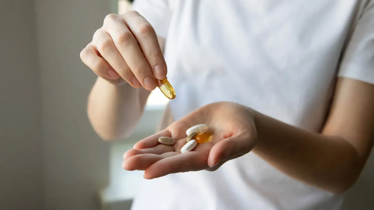 Frau hält mehrere Vitamin-Tabletten in der Hand und nimmt mit der anderen Hand eine Tablette auf