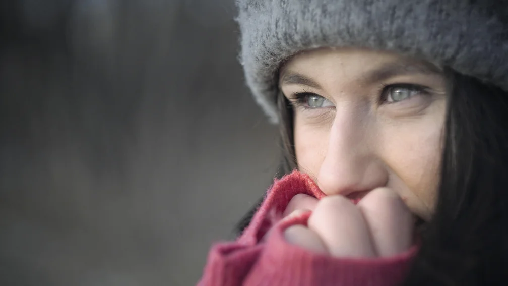 Frau mit Wintermütze hält sich die Hände vor den Mund