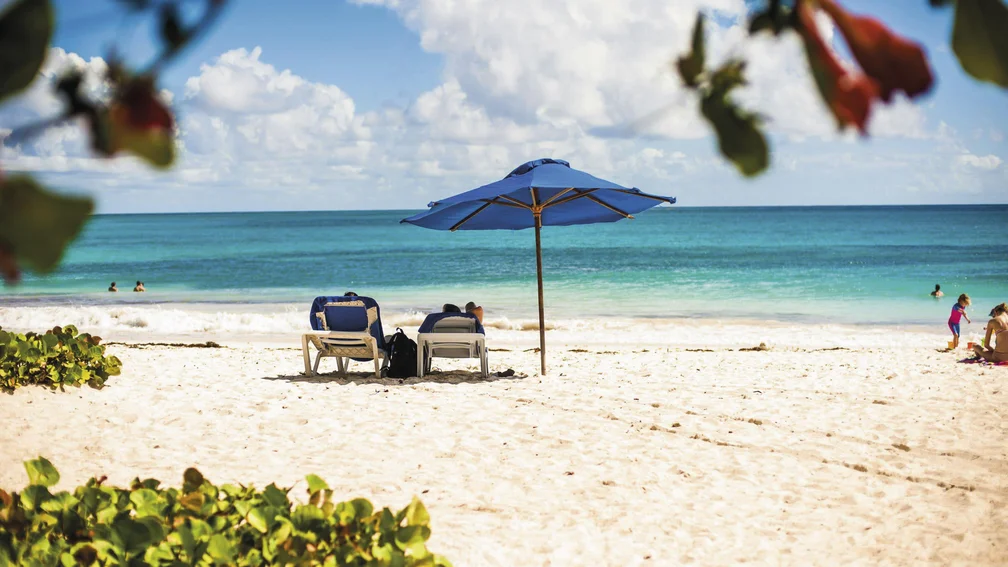 Karibischer Strand mit zwei Liegestühlen unter einem Sonnenschirm