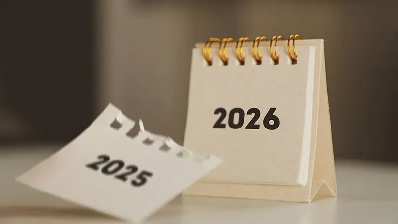 Abgerissenes Kalenderblatt mit Jahreszahl 2025 vor einem Kalender mit Jahreszahl 2026