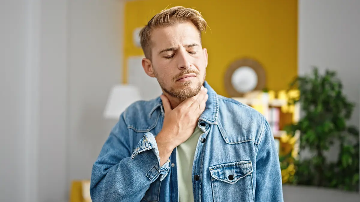 Junger Mann, der zu Hause an Halsschmerzen leidet.