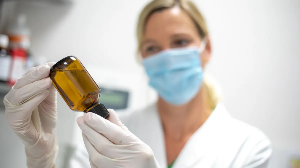 PTA steht in der Rezeptur und hält eine Braunglasflasche gefüllt mit Flüssigkeit verkehrt herum in den Händen