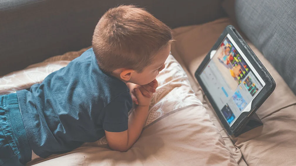 kleiner Junge liegt auf einem Bett und schaut ein Cartoon auf einem Tablet