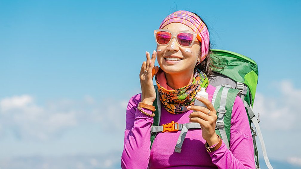 Wanderin in bunter Kleidung trägt Sonnencreme auf ihr Gesicht auf