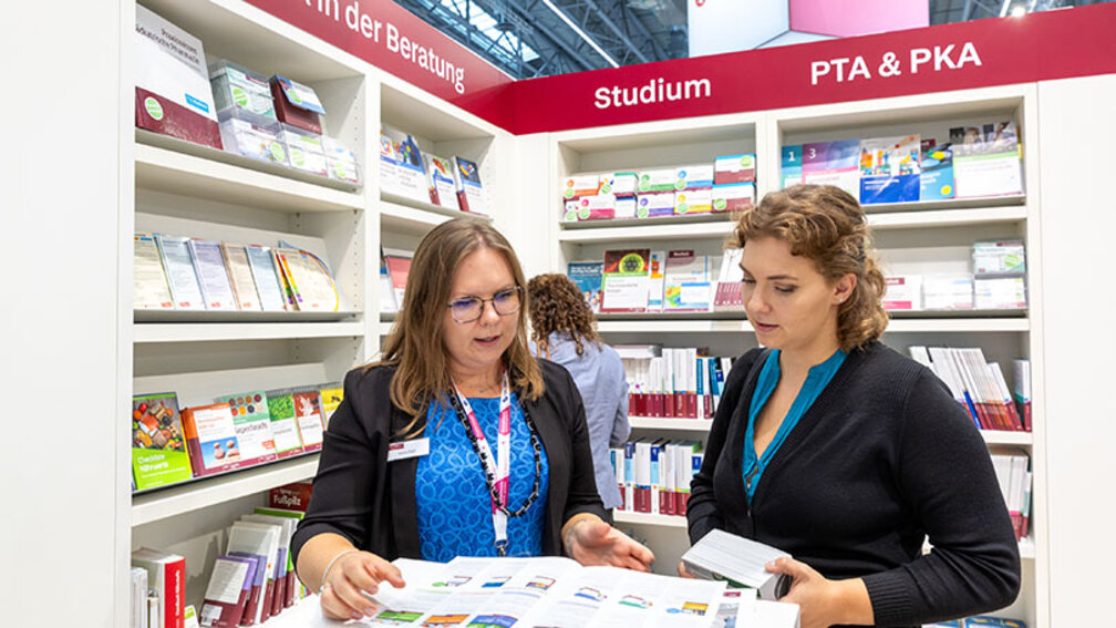 Zwei Frauen betrachten Katalog des DAV auf expopharm 2023