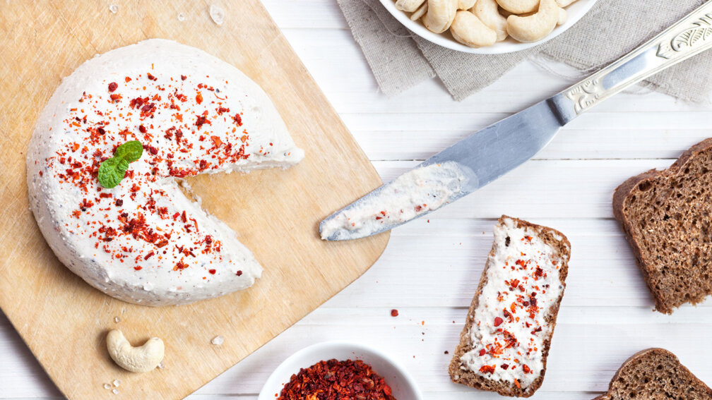 Runder Cashewkäse, daneben liegt eine Scheibe Brot