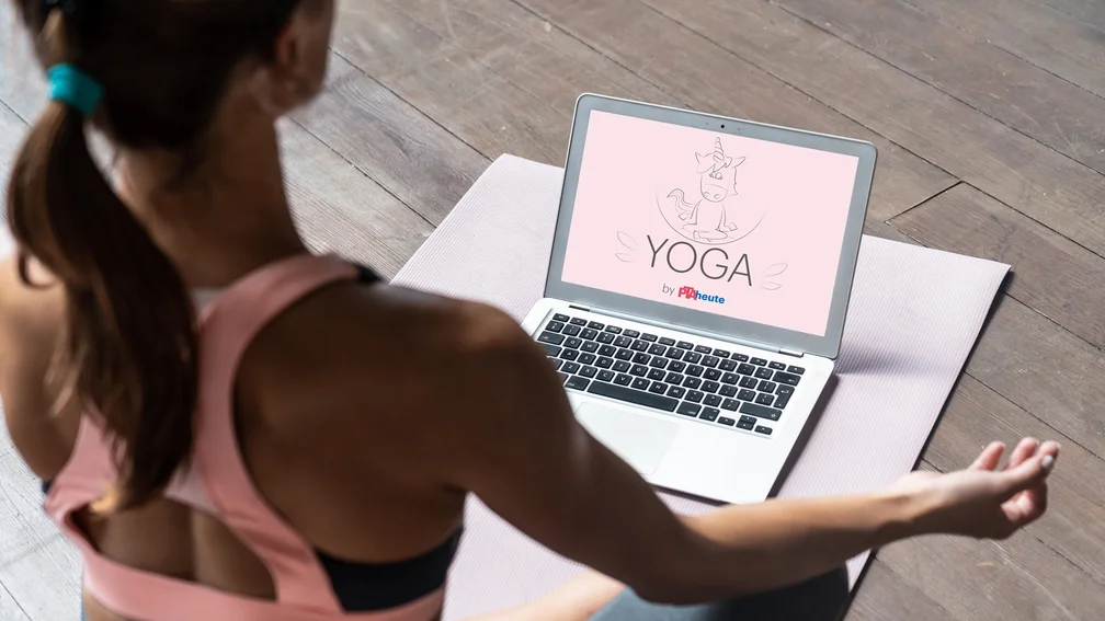 Frau sitzt vor Laptop und macht Yoga