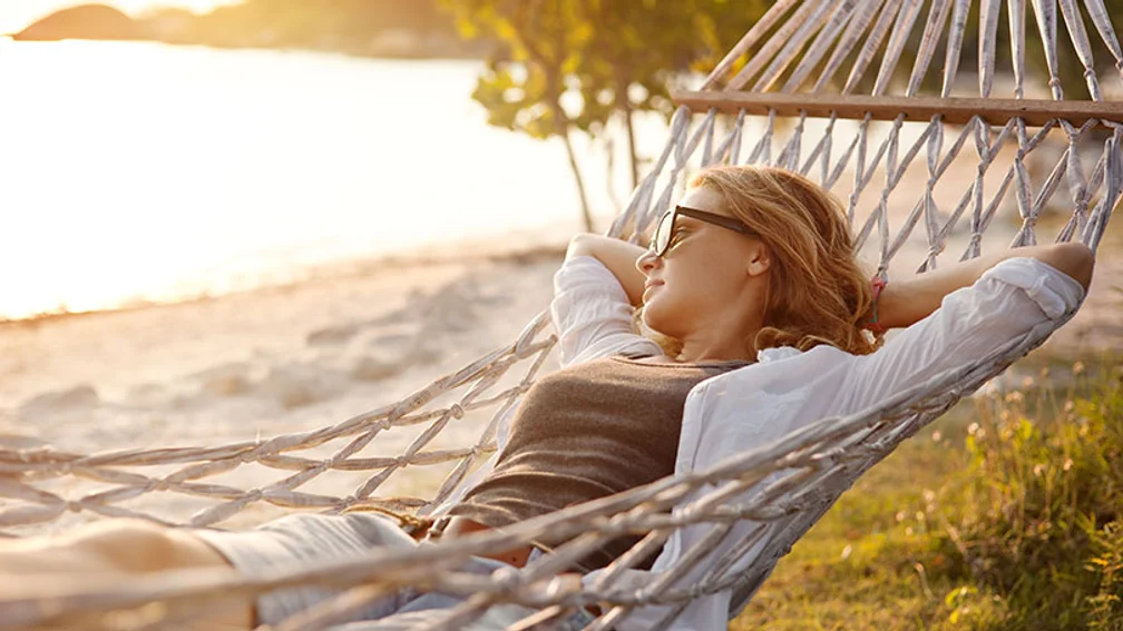 Blonde Frau liegt in einer Hängematte am Strand und beobachtet den Sonnenuntergang
