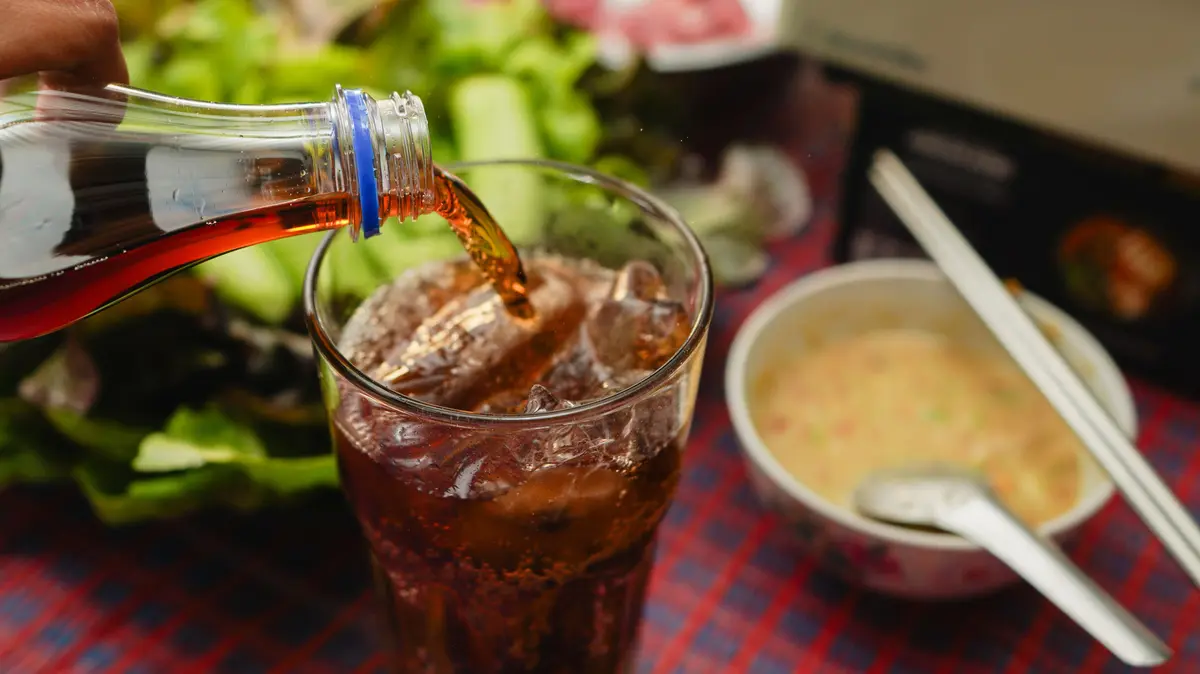 Glas wird mit Cola befüllt; im Hintergrund steht Essen