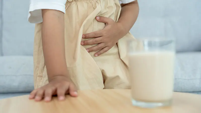 Kind hält Hand auf schmerzenden Bauch, vor ihm ein Glas Milch