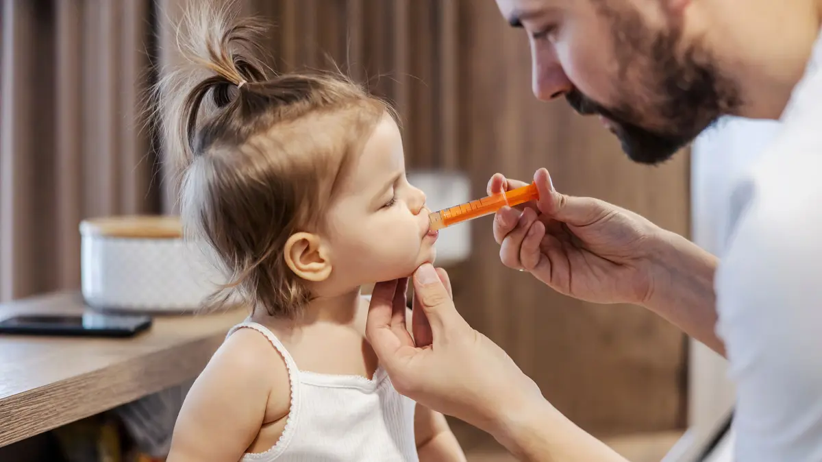 Vater verabreicht kranker Tochter Medizin über eine orale Dosierspritze