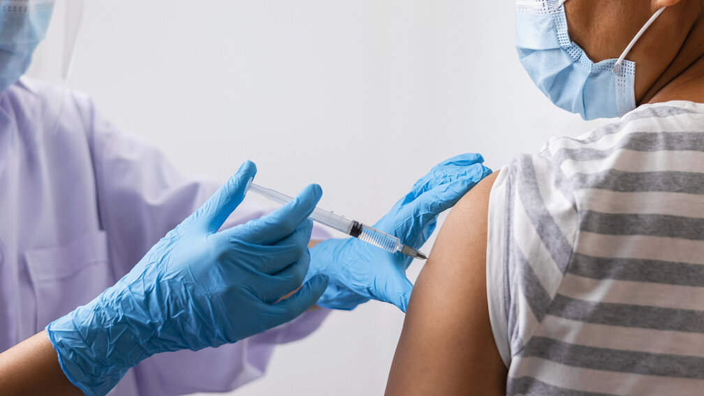 blau behandschuhte Hand sticht Impfspritze in Oberarm