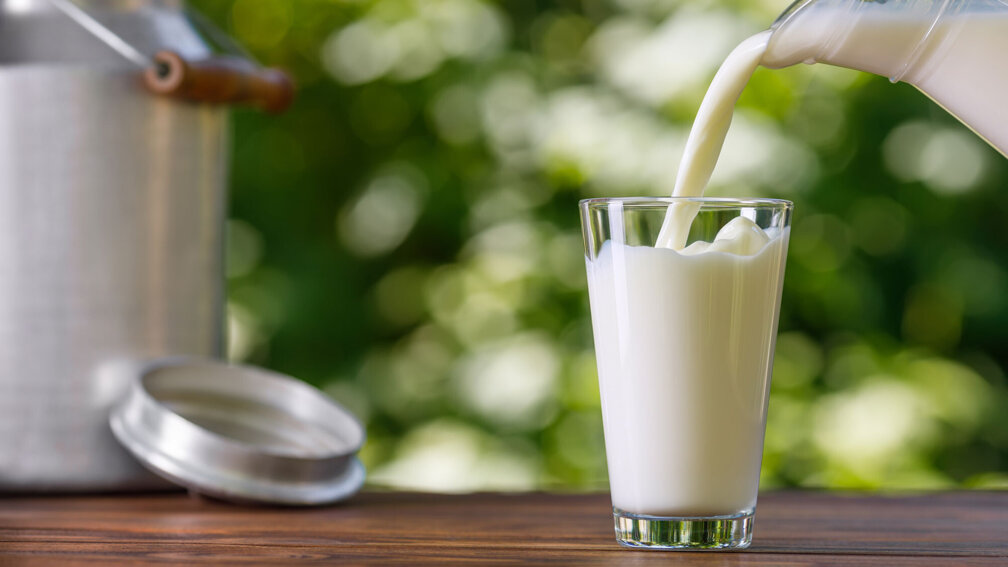 Milch wird aus einer Glaskaraffe in ein Glas eingeschenkt