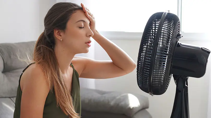 Junge Frau sitzt schwitzend vor Ventilator