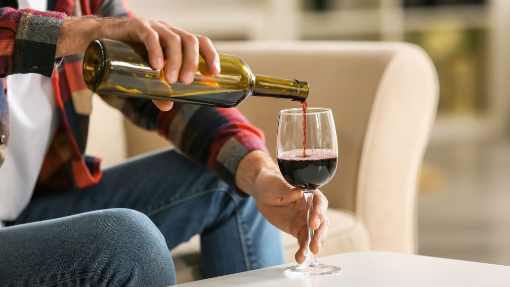 Mann schenkt sich aus einer Weinflasche ein Glas Wein ein