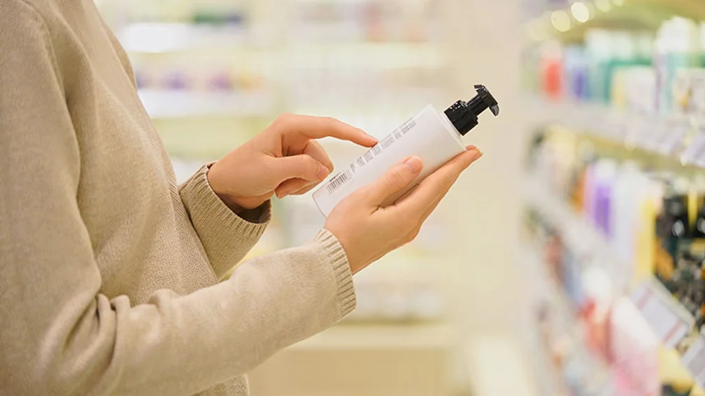 Frau hält in der Drogerie einen weißen Creme-Spender in der Hand und betrachtet das Kleingedruckte