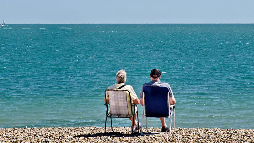 Ein älteres Pärchen sitzt in Klappstühlen am Steinstrand und schaut aufs Meer