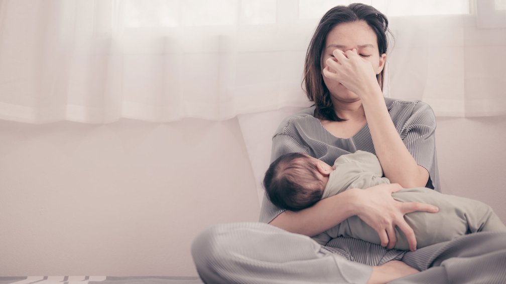 Frau sitzt auf dem Sofa und hält Säugling im Arm