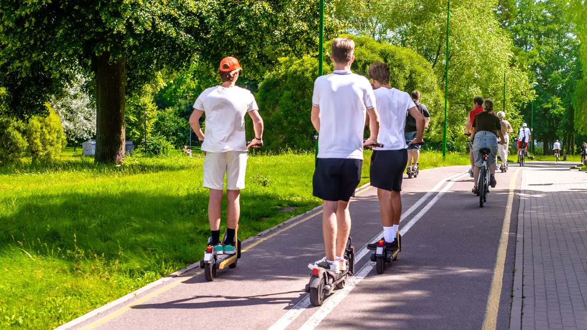 drei Jugendliche fahren auf E-Scootern, vor ihnen fahren zwei Fahrräder