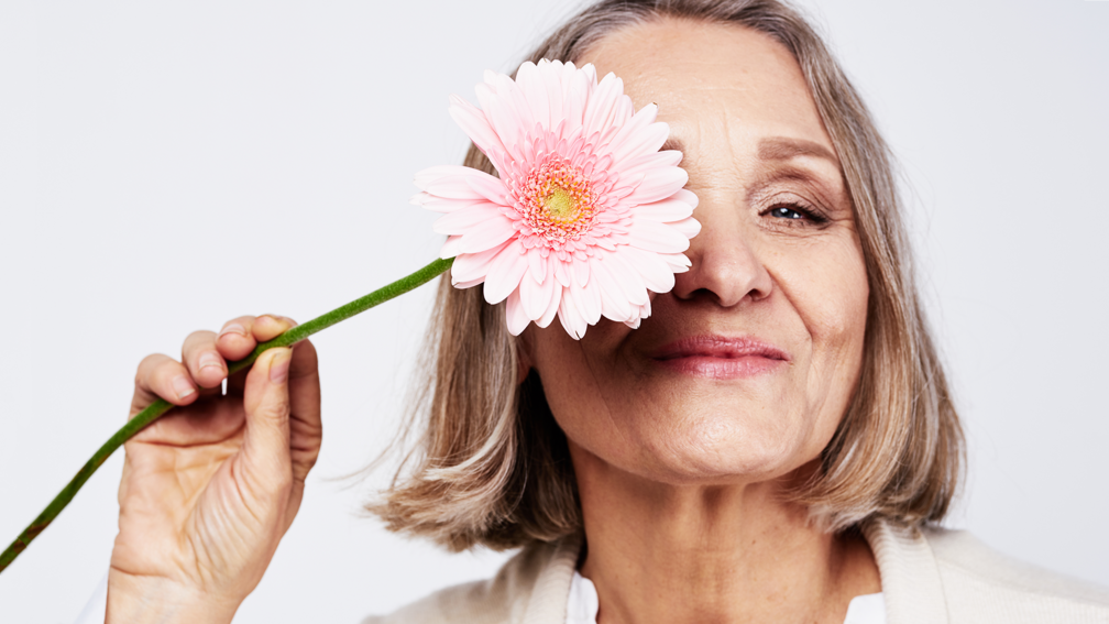 Ältere Frau hält rosane Gerbera vors Gesicht