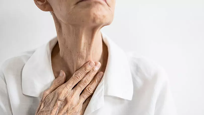 Seniorin legt Hand an Kehlkopf