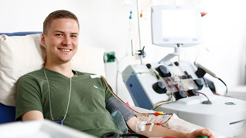 Junger Mann lächelt während Blutzellentnahme in die Kamera