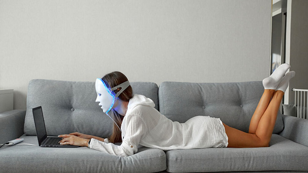 Frau mit Lichtmaske auf Gesicht liegt auf Sofa