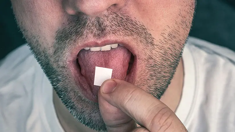 Mann mit Dreitagebart legt Blotterpapier auf seine Zunge