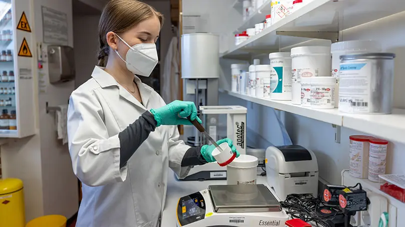 PTA mit FFP2-Maske steht im Apothekenlabor und rührt Creme an