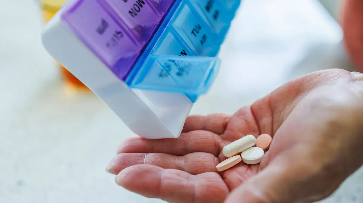 Tablettenbox, aus der vier tabletten in eine Hand gegeben werden