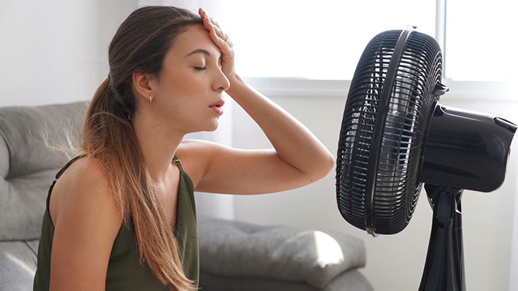 Junge Frau sitzt schwitzend vor Ventilator
