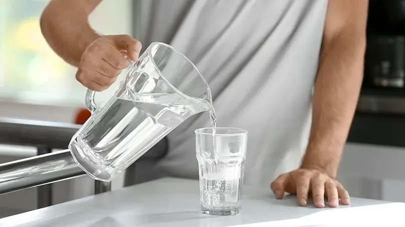 Mann schenkt sich ein Glas Wasser ein