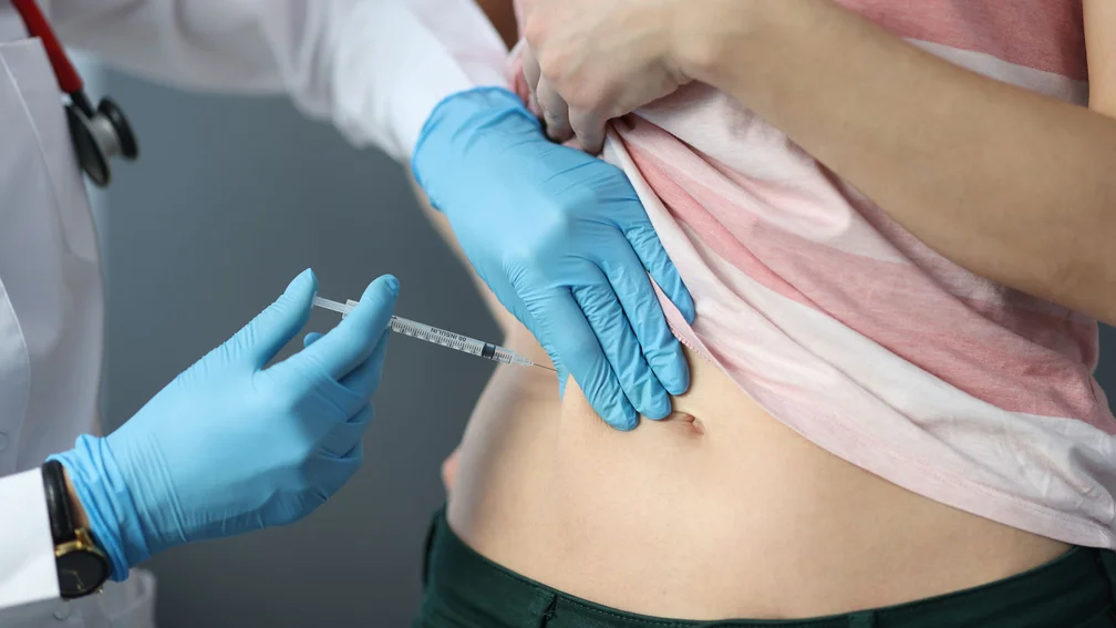 Ärztin injiziert eine Spritze in die Bauchfalte einer Patientin