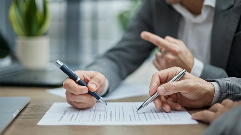 Zwei Personen zeigen mit Stift auf Dokument auf Tisch