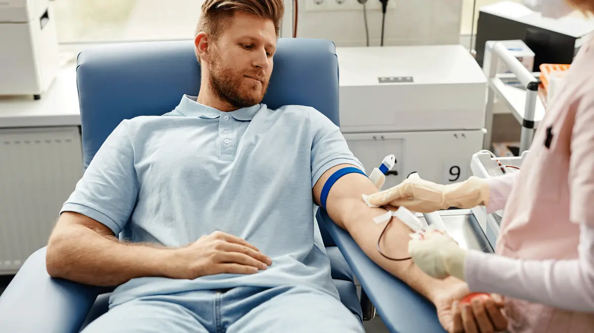 junger Mann liegt auf einem Stuhl während ihm Blut abgenommen wird