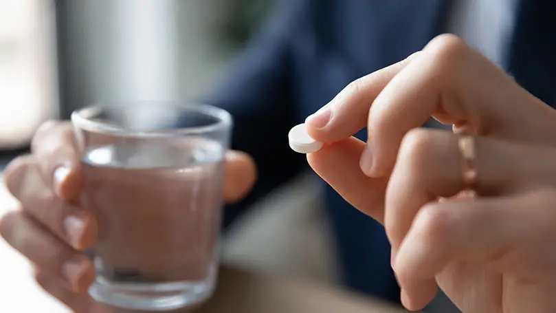 Nahaufnahme auf männliche Hände, die ein volles Wasserglas und eine weiße Tablette halten