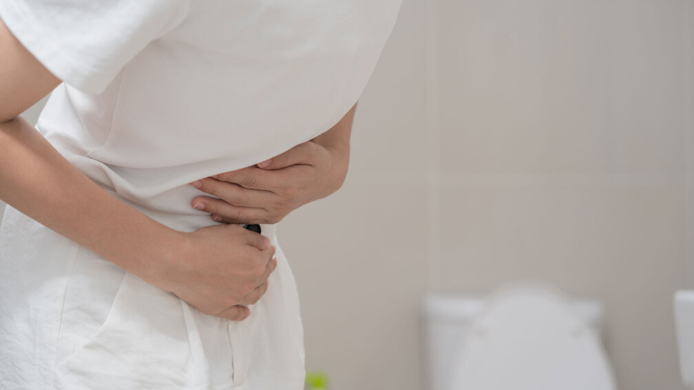Frau fasst sich an den Bauch, Toilette im Hintergrund sichtbar
