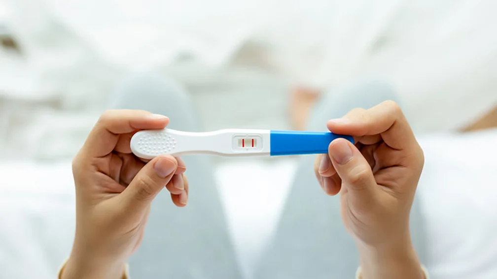 zwei weibliche Hände halten einen positiven Schwangerschaftstest