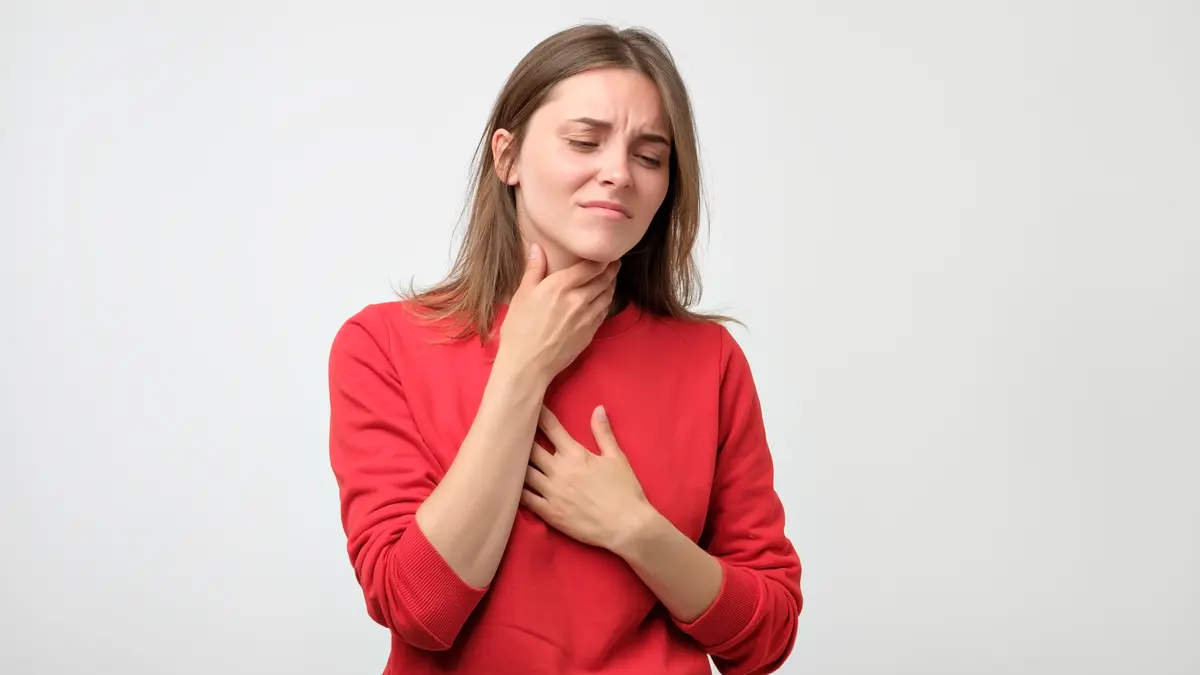 Junge Frau in rotem Pullover, die unter Halsschmerzen leidet.