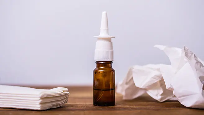 Nasenspray in Braunglasflasche auf Holzuntergrund neben Taschentüchern