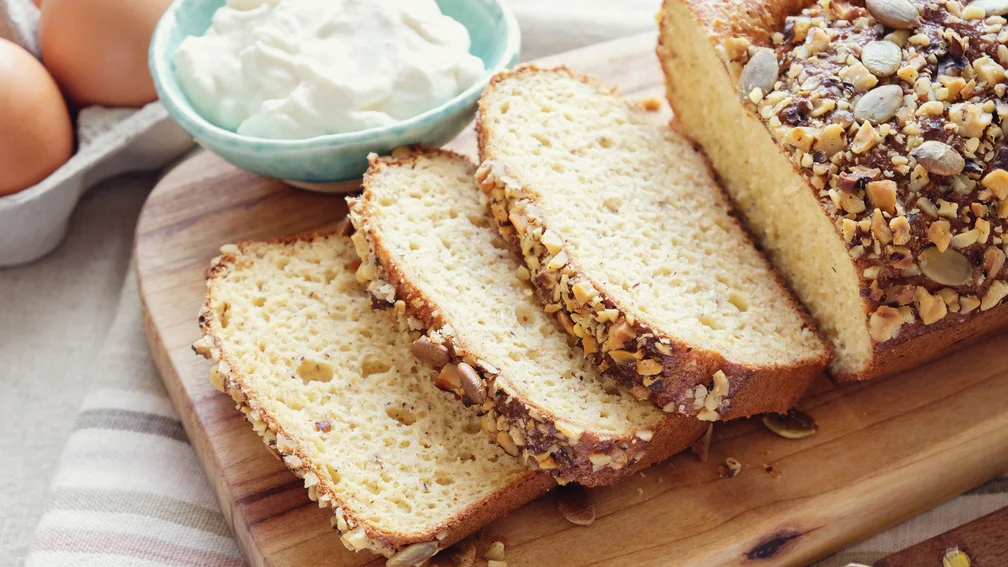 aufgeschnittenes Brot liegt auf einem Holzbrett, dahinter steht ein Schälchen mit Margarine und Eier
