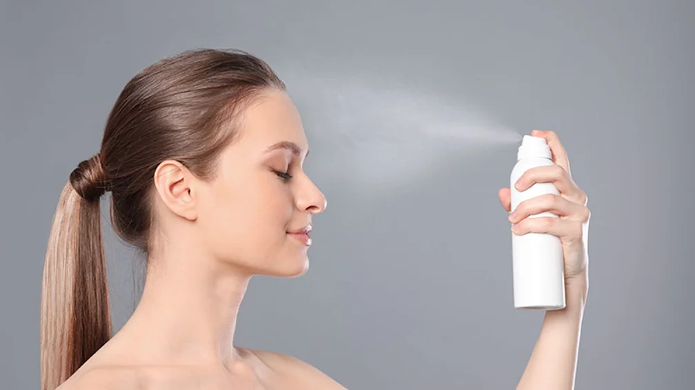 Langhaarige Frau sprüht sich mit geschlossenen Augen Spray ins Gesicht