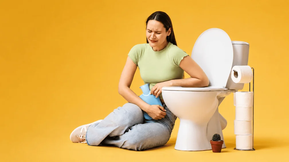 Frau die Schmerzen im Unterleib hat und neben der Toilette sitzt