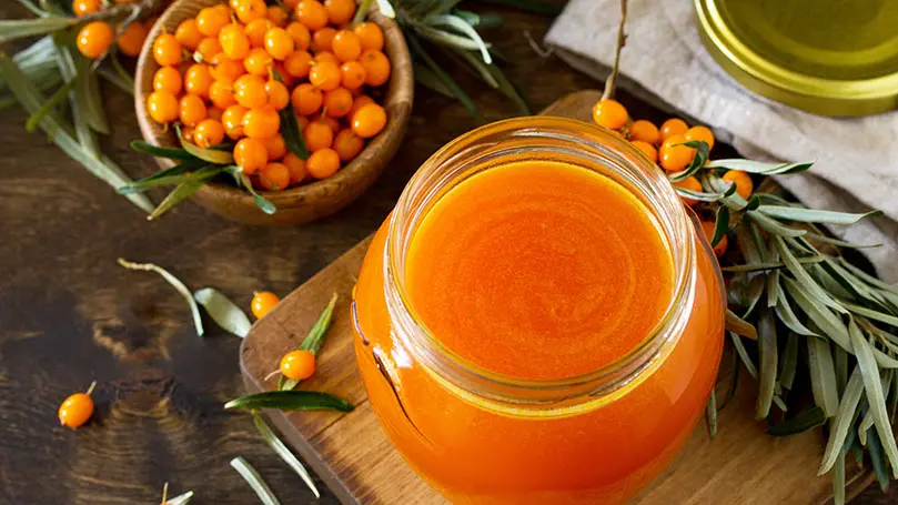 Glas mit Sanddornsaft neben Sanddorn-Früchten auf Holzuntergrund