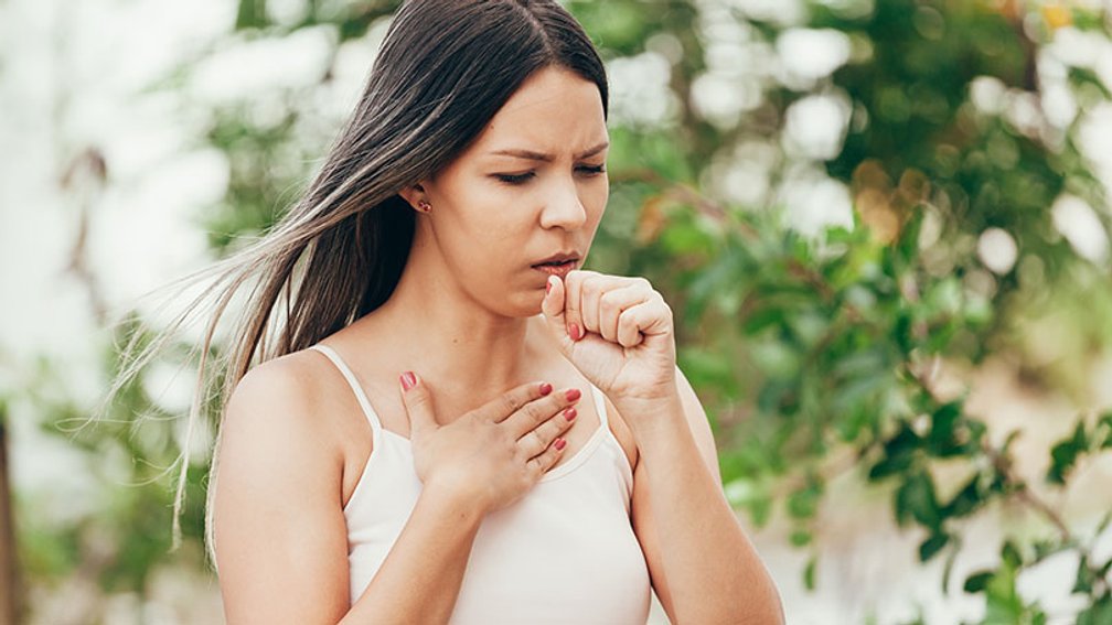 junge, dunkelhaarige Frau Husten unter Bäumen stehend