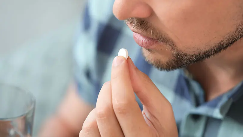 Nahaufnahme auf den Mund eines Mannes, vor dem eine Hand mit einer Tablette gehalten wird