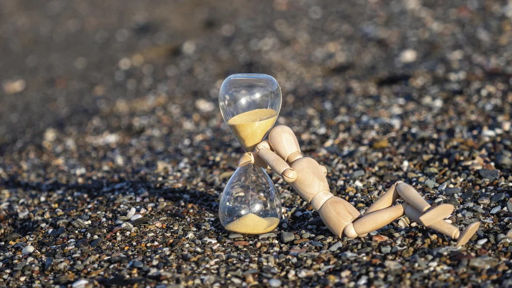 Holzfigur liegt an einer Sanduhr