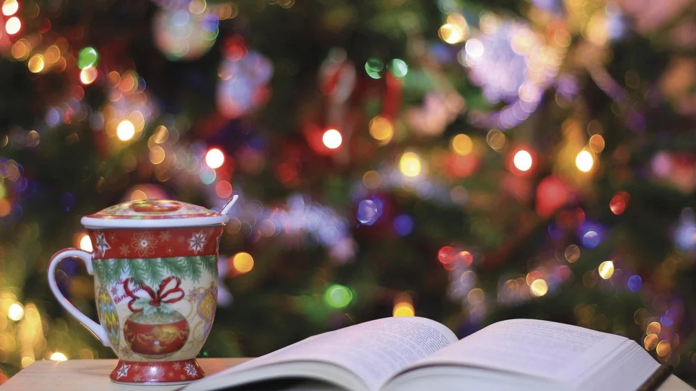 Tasse und Buch vor leuchtendem Weihnachtsbaum