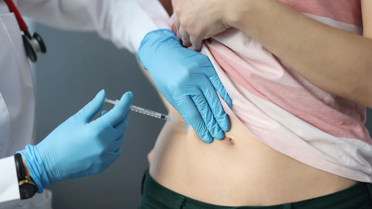 Ärztin injiziert eine Spritze in die Bauchfalte einer Patientin